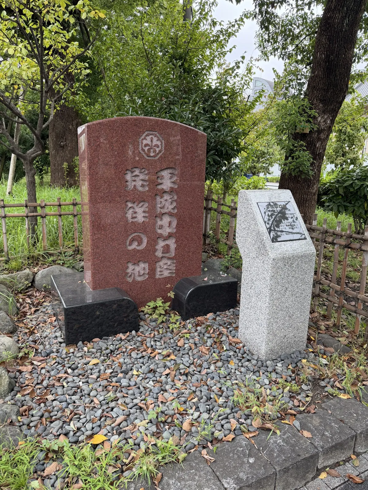 赤御影石の「平成中村座 発祥の地」碑と、右に立つ白御影の銘板の石柱